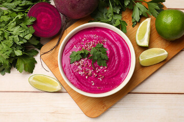 Tasty beetroot hummus in bowl and products on light wooden table, flat lay