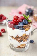 Tasty yogurt with fresh berries, granola and mint in glass on gray textured table, closeup