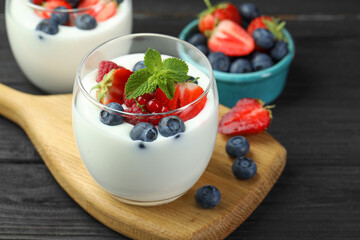 Tasty yogurt with fresh berries and mint in glasses on black wooden table, closeup