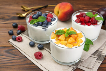 Tasty yogurt with fresh berries, fruits and mint in glasses on wooden table, closeup