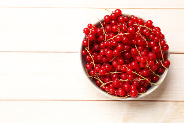 Fresh red currant berries in bowl on white wooden table, top view. Space for text
