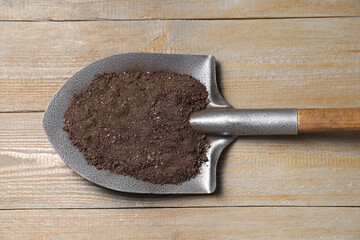 Metal shovel with soil on wooden table, top view
