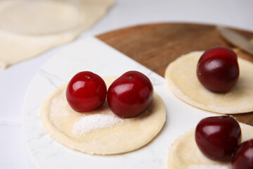 Process of making dumplings (varenyky) with cherries. Raw dough and ingredients on white table, closeup