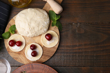 Process of making dumplings (varenyky) with cherries. Raw dough and ingredients on wooden table, flat lay. Space for text