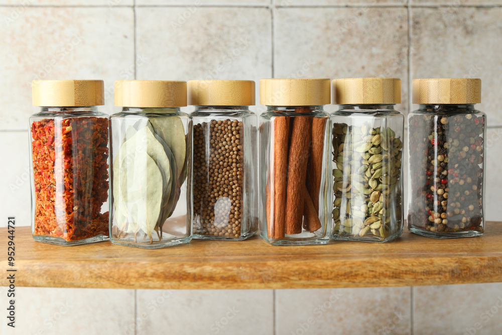 Wall mural different spices in glass jars on wooden shelf, closeup