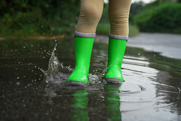 Little girl wearing green rubber boots walking in puddle outdoors, closeup