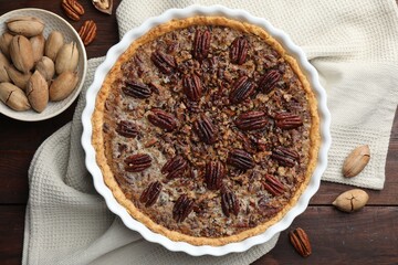 Delicious pecan pie in baking dish and fresh nuts on wooden table, flat lay