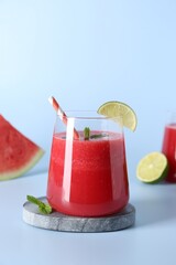 Tasty watermelon drink in glass, mint and fresh fruit on light blue background