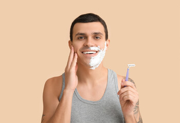 Handsome young man with razor and shaving foam on his face against beige background