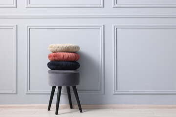 Stylish stool and cushions near light grey wall indoors, space for text