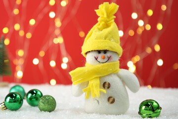 Cute decorative snowman and Christmas balls on artificial snow against blurred lights