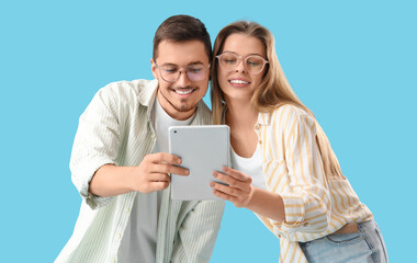 Young couple in eyeglasses using tablet computer on blue background