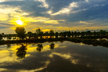 A breathtaking sunset casts golden hues over a tranquil pond near Mengare, Gresik, Indonesia