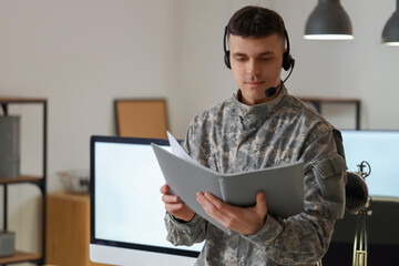 Young male soldier in headset with journal at headquarters