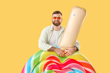 Young man with inflatable mattress in shape of lollipop on yellow background