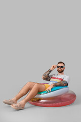 Young man with inflatable rings on grey background