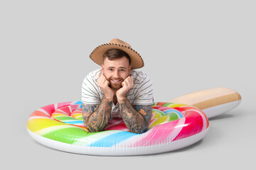 Young man with inflatable mattress in shape of lollipop on grey background