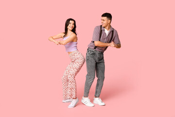 Happy young couple dancing on pink background