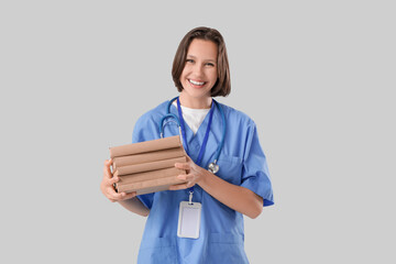 Female medical intern with books on light background