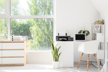 Modern workplace with laptop, printer and plants in light office