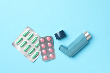 Asthma inhaler and pills on light blue background, flat lay