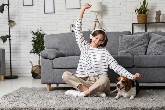 Young woman in headphones with cute Beagle dog sitting on floor near sofa at home