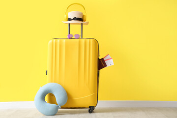 Packed suitcases with neck pillow, hat and passport near yellow wall