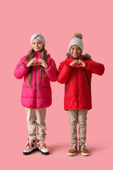 Cute little happy children in winter clothes showing hearts gesture on pink background