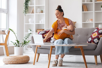 Young mother with cute little baby in sling and laptop sitting on sofa at home