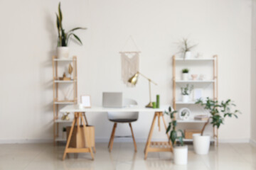 Interior of modern stylish workspace with shelving units and laptop on table, blurred view