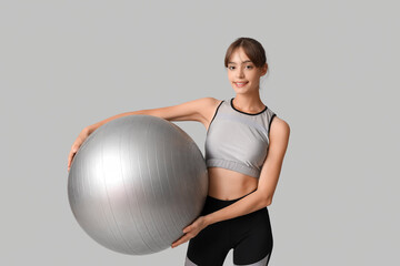 Young woman with fitball on  grey background