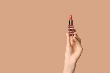 Female hand with lipstick on brown background