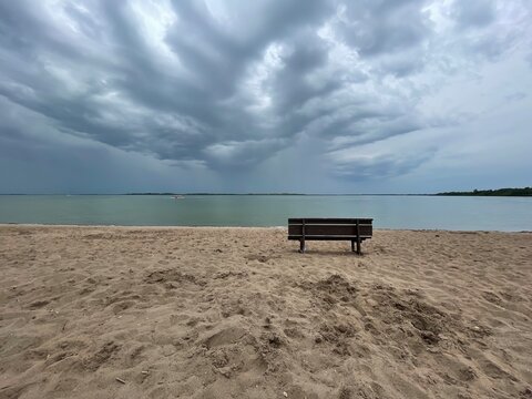 Banca vac&iacute;a en playa con tormenta aproxim&aacute;ndose. 