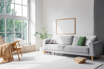 Interior of stylish room with grey sofa, armchair and books on floor near window