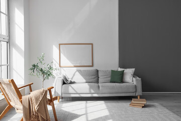 Interior of stylish room with grey sofa, armchair and books on floor near window