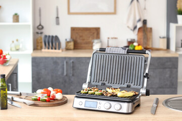 Modern electric grill with fresh tasty vegetables on table in kitchen