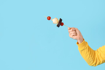 Male hand with tasty fresh vegetables skewer on blue background