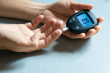 Woman's hands checking diabetes and hyperglycemia with digital blood sugar meter. Healthcare and...