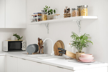 Interior of light kitchen with sink, shelf and utensils