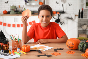 Teenage African-American boy with paper pumpkin making Halloween decorations at home