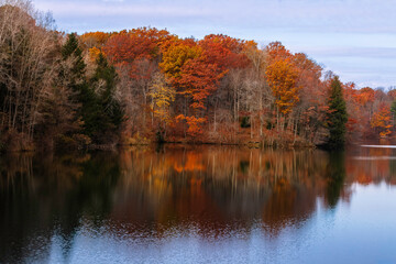 Autumn colorful foliage over lake with beautiful woods in red and orange colour reflecting in the water