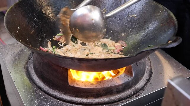 A chef is cooking rice noddle over a charcoal fire.