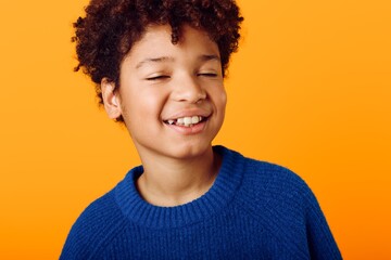 Cheerful young african american boy with curly hair smiling brightly against a vibrant orange background