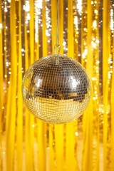 Silver disco ball hanging with lighting reflections on yellow background