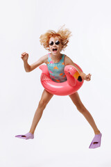 A child in black glasses and a blue-orange swimsuit with an inflatable duck ring on a white background. The concept summer holiday on the beach or pool.