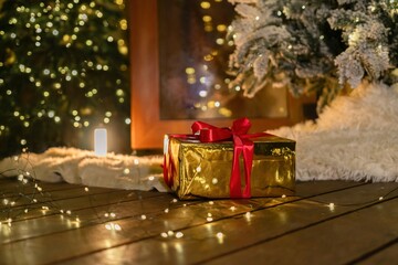 Gift, Christmas, Lights - A gold gift box with a red ribbon sits on a wooden floor decorated with...