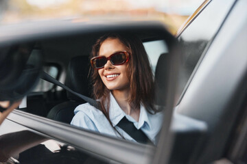 Woman, sunglasses, car, rearview mirror a woman wearing sunglasses sits in the rearview mirror of a car with her hand on the steering wheel, smiling confidently in the sunlight