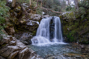 A tranquil waterfall nestled within a lush, moss-covered forest in Villa La Angostura, Patagonia, Argentina. The serene cascade of water flows over rugged rocks into a crystal-clear pool.