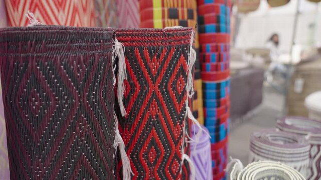 A close-up view of intricately woven pattern rugs displayed in a bustling street market. The rich colors and textures highlight the craftsmanship and local artistry.