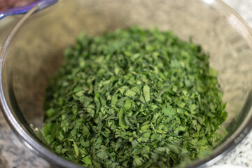 Chopped parsley in glass bowl along with other ingredients necessary to prepare chiles en nogada